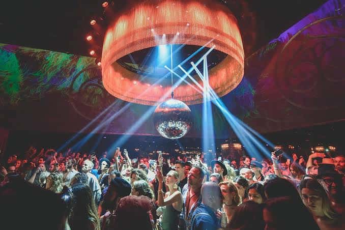 Interior del Club Chinois con gran lámpara circular y gente bailando bajo luces de neón