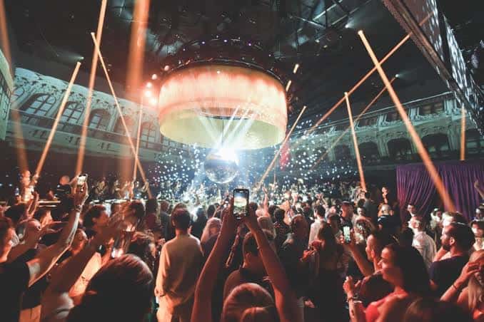 Escena nocturna en el club con confeti cayendo y público celebrando bajo luces cálidas