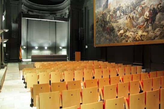 Vista del auditorio vacío con las butacas de madera y el escenario