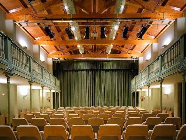 Interior del auditorio con butacas y cortina verde cerrada