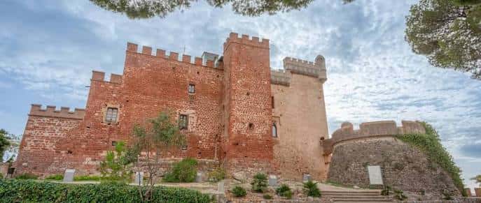 Vista panorámica del Castillo de Castelldefels con sus torres rojizas y murallas bajo un cielo parcialmente nublado