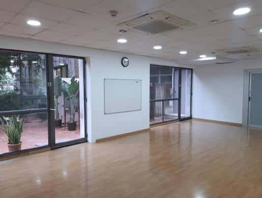 Sala polivalente con suelo de madera y grandes ventanales, ideal para talleres o reuniones
