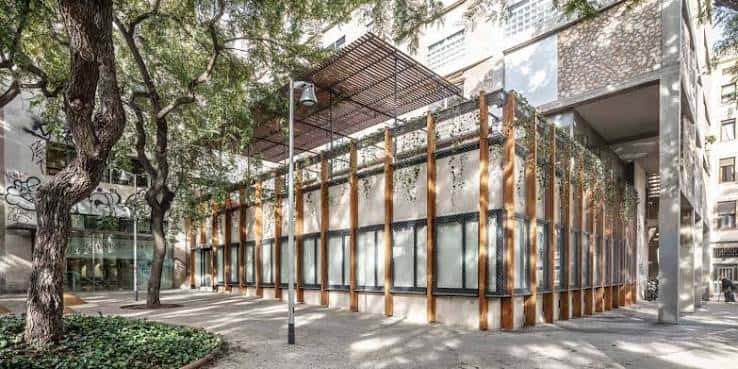 Fachada exterior del Centre Cívic Drassanes con estructura de madera y vegetación, en un entorno urbano arbolado