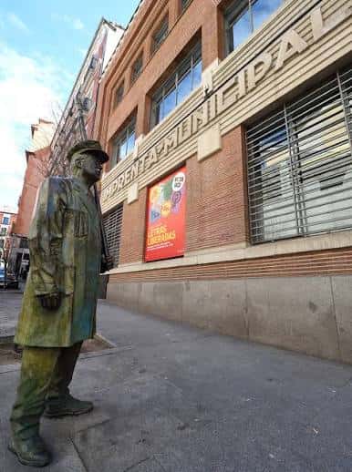 Vista lateral del edificio con estatua y cartel de Artes del Libro