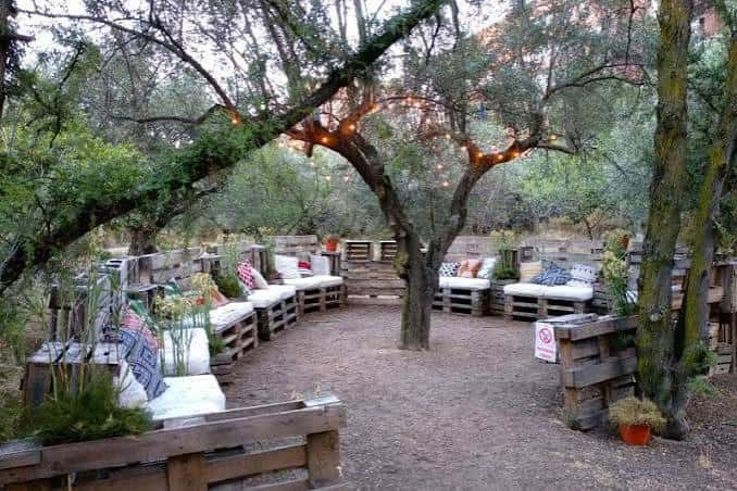 Área de eventos con sofás rústicos y iluminación cálida entre árboles