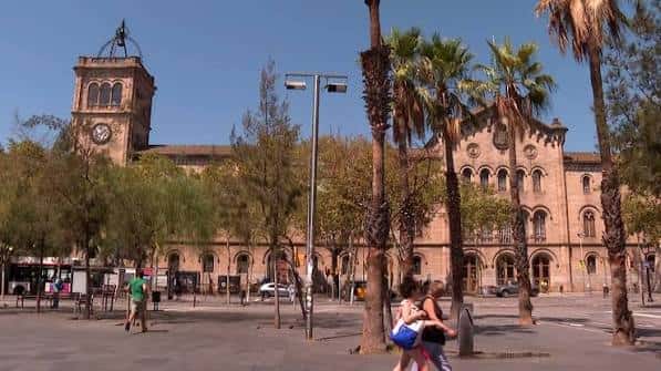 Fachada de la Universidad de Barcelona con la torre del reloj y palmeras en primer plano