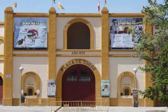 Entrada monumental de la Plaza de Toros de Huesca con carteles de eventos y banderas
