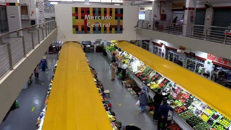 Vista interior del Mercado Central mostrando puestos de frutas y verduras con toldos amarillos y cartel de identificación