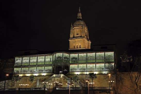 Fachada iluminada de la Casa Lis por la noche, destacando sus ventanales de cristal coloreado