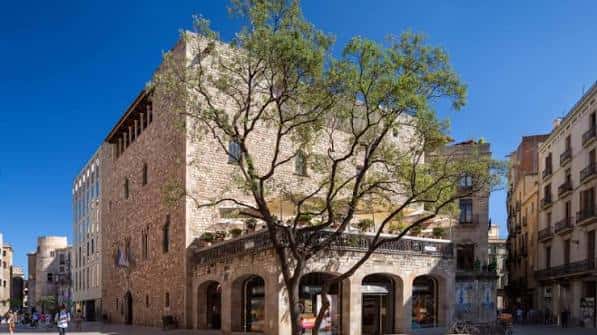 Vista exterior del Reial Cercle Artístic con fachada de piedra y árbol en primer plano