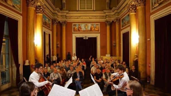 Sala de conciertos con músicos en vivo y público sentado bajo techos decorados