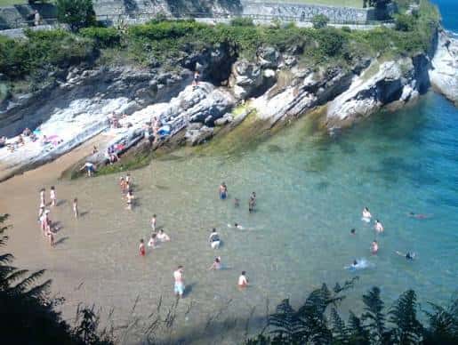 Playa de Los Molinucos con personas nadando y rocas costeras