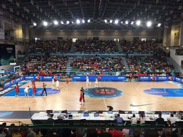 Interior del pabellón durante un partido de baloncesto con público en las gradas y cancha iluminada