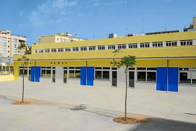 Fachada amarilla y azul del colegio con patio exterior