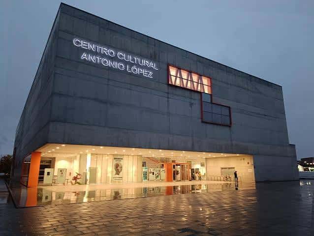 Fachada iluminada del Centro Cultural Antonio López al atardecer con reflejos en el suelo mojado