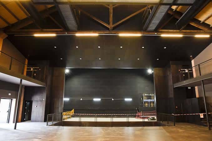 Interior del auditorio con escenario, techo de vigas de madera y sistema de iluminación profesional