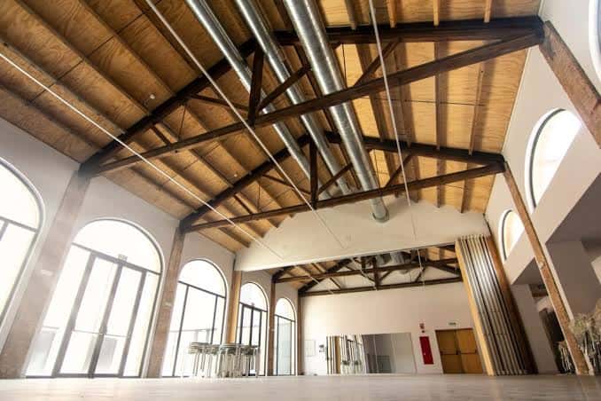 Espacio interior amplio con techo de madera, vigas estructurales y grandes ventanales curvos