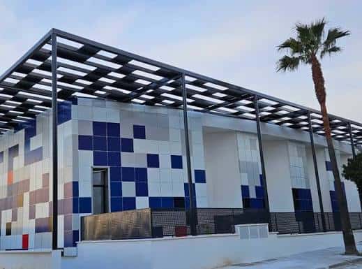 Vista exterior del Centro Polivalente con su distintiva fachada de azulejos multicolores y estructura metálica