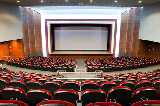 Sala de cine moderna con pantalla grande y butacas rojas y negras en disposición semicircular