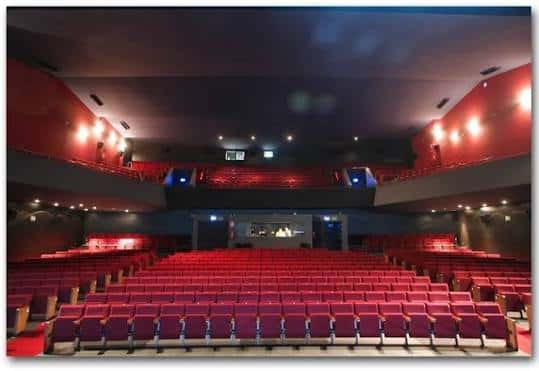 Interior del auditorio con butacas rojas dispuestas en gradas y escenario iluminado