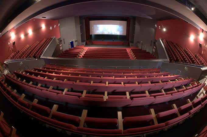Vista panorámica del salón de actos con butacas rojas y pantalla de proyección en el escenario