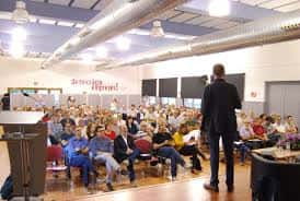 Interior del auditorio durante un acto cultural con público sentado y orador en el escenario