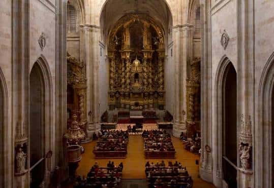 Interior de la iglesia con retablo dorado y congregación sentada en bancos de madera