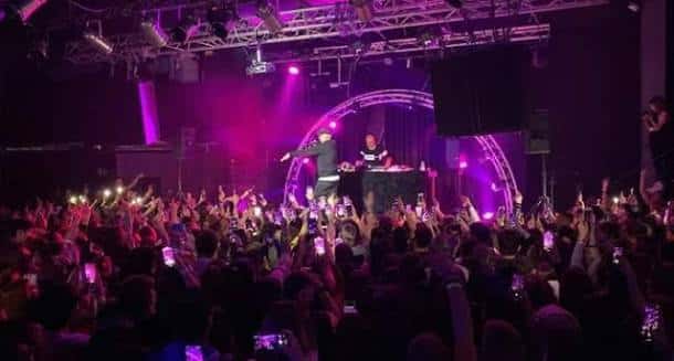 DJ actuando frente a una multitud con luces púrpuras y arco de escenario