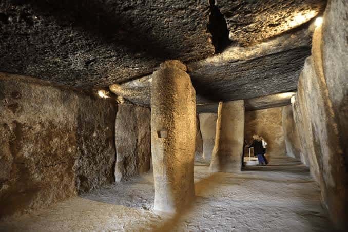 Interior del dolmen con grandes piedras verticales y techo de losa, con turistas en el fondo