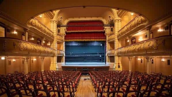 Vista frontal del escenario con cortina roja y platea del teatro