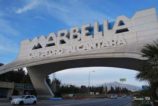 Detalle del Arco de Marbella con cielo azul y montañas al fondo