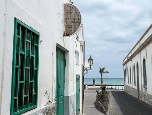Vista exterior de la fachada blanca y verde de La Recova Municipal con el mar al fondo
