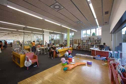 Sala infantil de la biblioteca con mobiliario colorido y niños leyendo