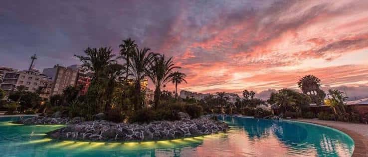 Vista panorámica del parque marítimo al atardecer con palmeras y piscina iluminada