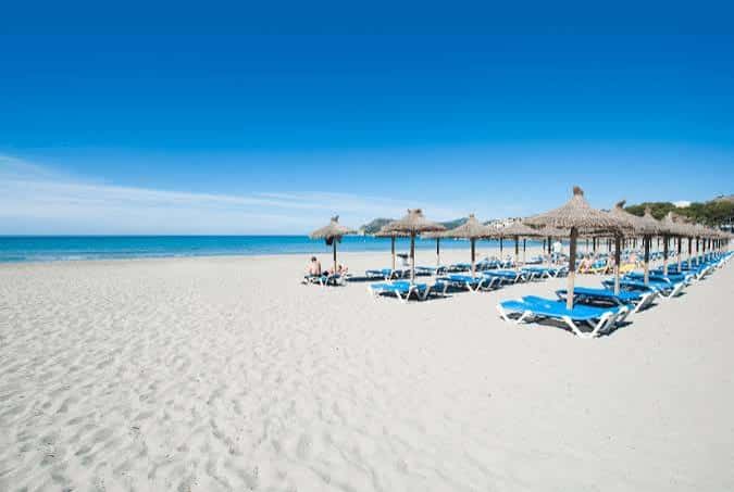 Playa Torà con hamacas y sombrillas de paja alineadas frente al mar azul