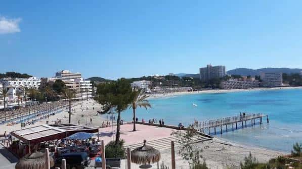 Vista panorámica de la playa Torà con muelle, palmeras y edificios costeros al fondo