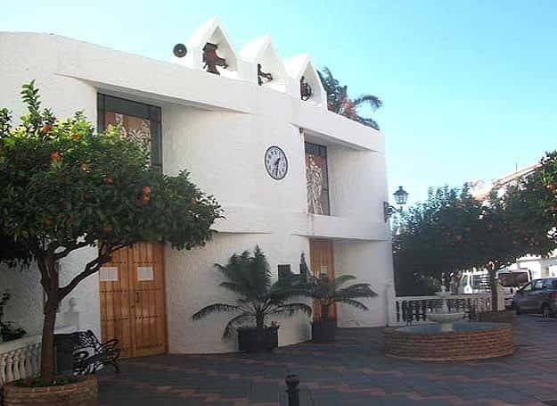 Fachada de la iglesia rodeada de naranjos y palmeras en un día soleado