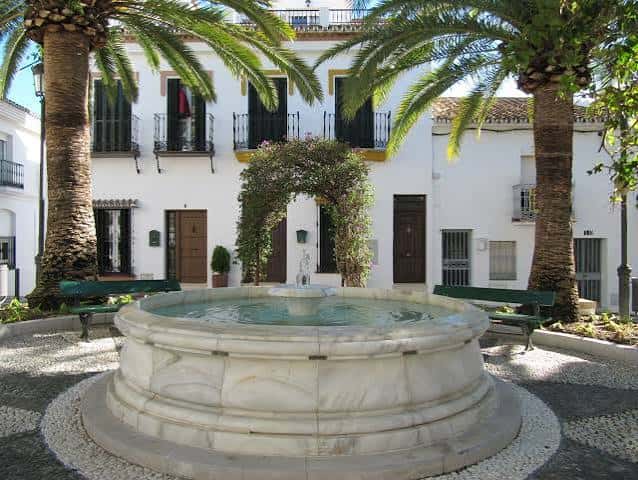 Fuente central de la plaza rodeada de palmeras y bancos verdes
