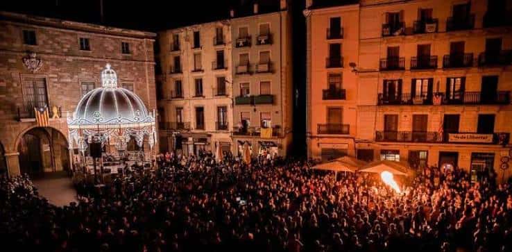 Vista nocturna de la plaza llena de público con una estructura iluminada en el centro