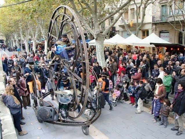 Espectáculo callejero con una gran estructura metálica en forma de rueda y un músico