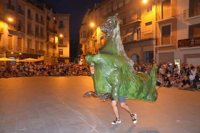 Artista con un disfraz de dragón verde actuando en una plaza durante la noche