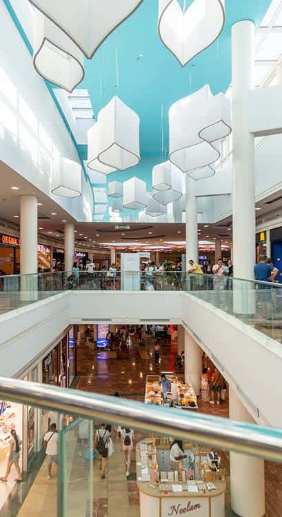 Interior del centro comercial con múltiples niveles, tiendas y decoración luminosa