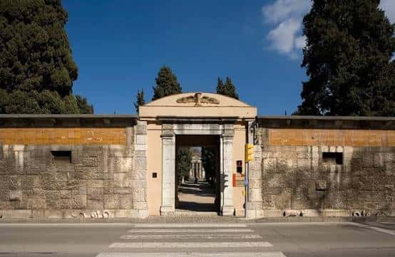 Fachada principal del cementerio con arco de acceso y muros de piedra bajo luz diurna