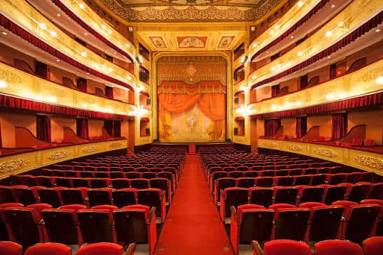 Escenario con telón dorado y vista frontal de las gradas del teatro
