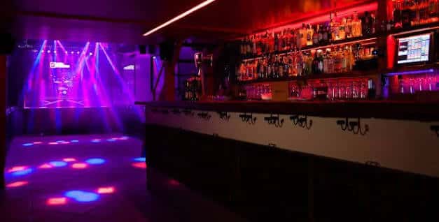 Interior del bar con estantería de bebidas y luces de discoteca