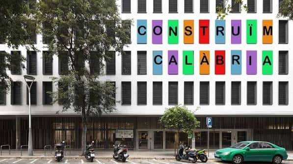 Fachada del edificio Calàbria 66 con el letrero 'CONSTRUÏM CALÀBRIA' y árboles en primer plano