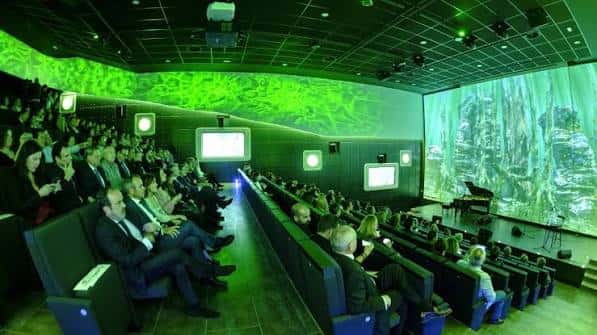 Interior del auditorio con proyección inmersiva verde y público sentado