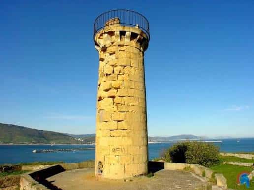 Primer plano de la torre del faro del Fuerte de La Galea con vistas al mar y montañas al fondo