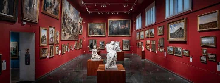 Galería de arte con paredes rojas y obras expuestas