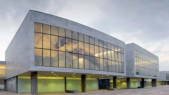 Fachada principal del edificio con estructura elevada y cristaleras que reflejan el cielo, ideal para eventos corporativos o culturales